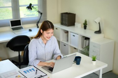 Parlak ve minimal çalışma alanında uzaktan kumanda için bilgisayar kullanan gülümseyen kadın.