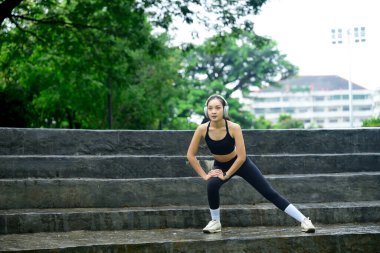 Siyah spor giyimli bayan sporcu antrenmandan önce ısınıyor, azimle egzersiz yapıyor..