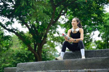 Antrenman sırasında mola veren bayan sporcu dışarıda taş merdivenlerde su şişesiyle oturuyor..