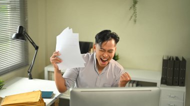 Mutlu ofis çalışanı işinde zafer kazanıyor, elinde belgelerle tezahürat yapıyor..