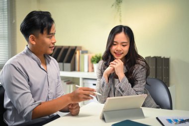 Ofiste birlikte çalışan iki meslektaşım dijital tablete bakarken fikirleri tartışıyor..