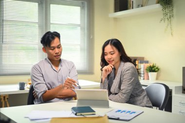 İki iş arkadaşı, dijital tablet üzerindeki verileri incelerken fikirleri tartışıyor..