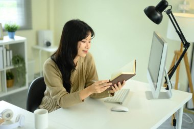 Dergiden notlar okurken ofis masasında çalışan genç bir kadın..