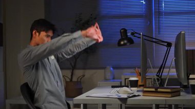 Loş bir ofiste saatlerce bilgisayar çalıştıktan sonra çalışma masasında uzanan yorgun bir ofis çalışanı..