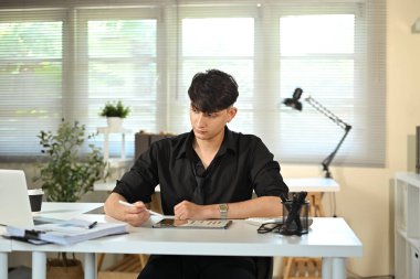 Genç işadamı dijital tablet üzerinde çalışıyor, modern ofiste grafikleri analiz ediyor..