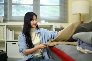 Genç bir kadın yaklaşan ev gezisi için bavullarını toplarken elbiselerini katlıyor..