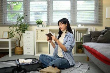 Pasaportunu kontrol eden bir yolcu, yanında gerekli eşyalarla dolu bir bavul..