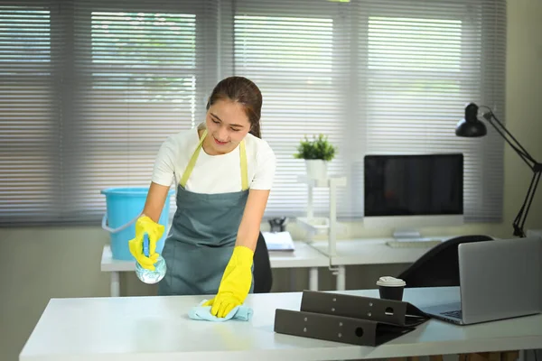 Gülümseyen kadın masasını sprey temizleyicisi ve bezle dezenfekte ediyor, temizlik ve hijyen kavramı.