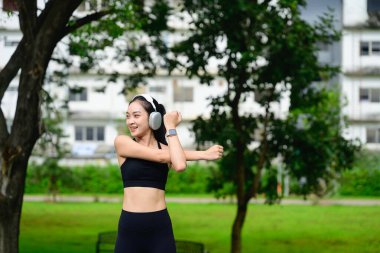 Açık hava antrenmanı sırasında vücudunun üst kısmını esneten gülümseyen bir sporcu..