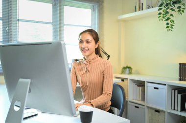 Parlak modern ofis bilgisayarında çalışan gülümseyen genç kadın..