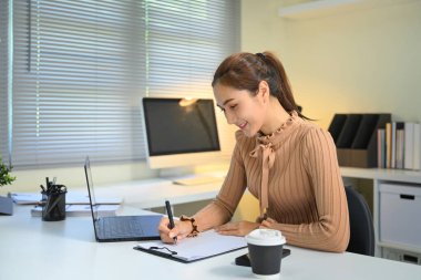 Gülümseyen iş kadını ev işyerinde çalışırken not alıyor.