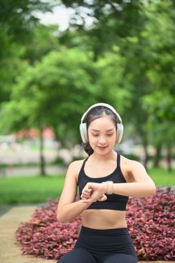 Kadın sporcu parkta kulaklık takarken akıllı seğirmeyle ilgili egzersiz verilerini kontrol ediyor..