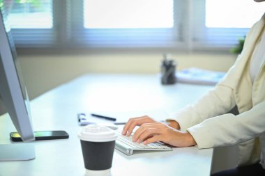 Modern bir ofis masasında, kablosuz klavyede kahve fincanıyla yazı yazan elleri kapatın..