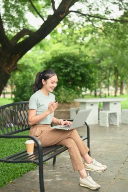 Parkta dizüstü bilgisayar kullanan genç kadın işçi, dijital göçebe kavramı.