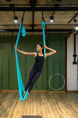 Havadan yoga salıncağıyla kendinden emin duran bayan sporcu, güç ve denge eğitimine odaklanıyor..