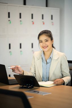 Ofiste dizüstü bilgisayar ve tabletle çalışırken kameraya gülümseyen kendine güvenen iş kadını.