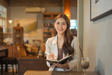 Samimi bir kafede otururken elinde defter ve kalemle gülümseyen iş kadını..