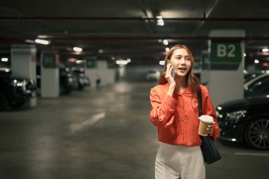 Bir yeraltı otoparkında elinde kahve fincanı tutarak konuşan bir iş kadını..
