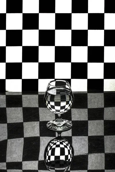 Abstract still life with a glass on a background of black and white cells — Stock Photo, Image
