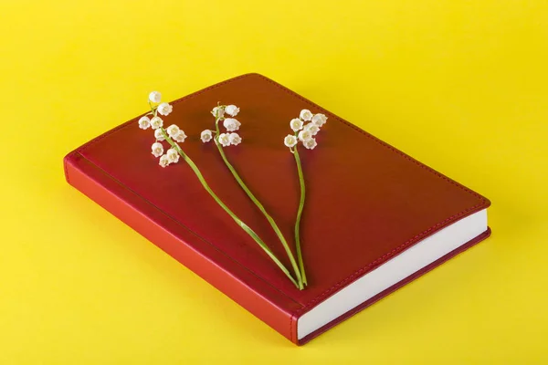 Red notepad with lily of the valley flowers on a yellow background