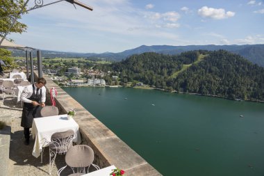 Bled, Slovenya - 15 Ağustos 2019: Slovenya'da bir gölün arka planında Bled Kalesi topraklarında bir garson ile bir kafenin parçası