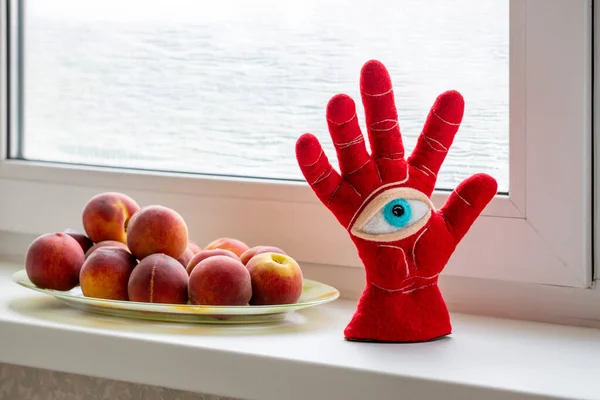 Protective amulet in the shape of an open palm and eye made of felted wool on a peach windowsill