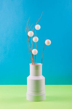 Dal ve beyaz toplarla dolu beyaz bir vazoda, renkli bir arka planda.