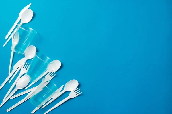 White single-use plastic knives, spoons, forks on a blue background. Say no to single use plastic. Environmental, pollution concept.