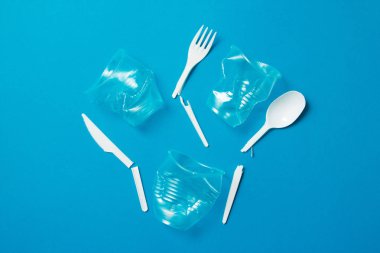 Mavi arka planda beyaz kırık plastik bıçaklar, kaşıklar, çatallar ve plastik pipetler. Tek kullanımlık plastiğe hayır de. Çevresel, kirlilik kavramı.
