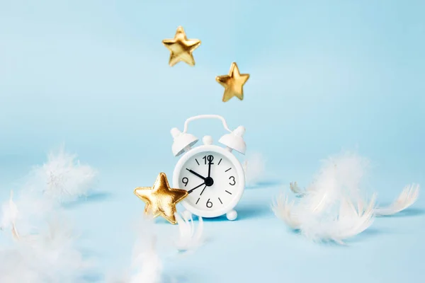 Retro alarm clock with gold stars and feathers on a blue background. Time to sleep concept