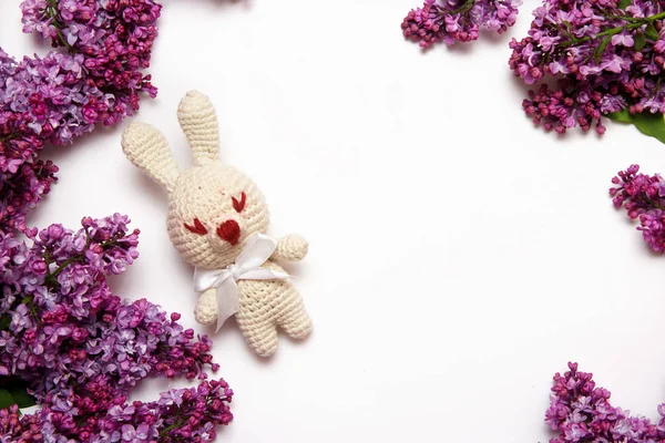 Lilac flowers with knitting toy rabbit on white background. Top view, flat lay, copy space.
