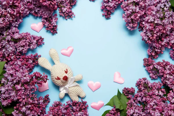 Lilac flowers with knitting toy rabbit on blue background. Top view, flat lay, copy space.