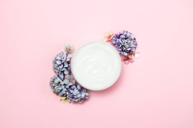 Pembe arka planda çiçekli bir kavanoz krema. Üstte görüntü.