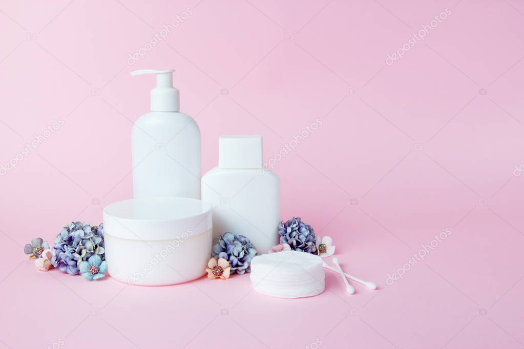 White jars of cosmetics with flowers on a pink background. Bath accessories. Face and body care concept