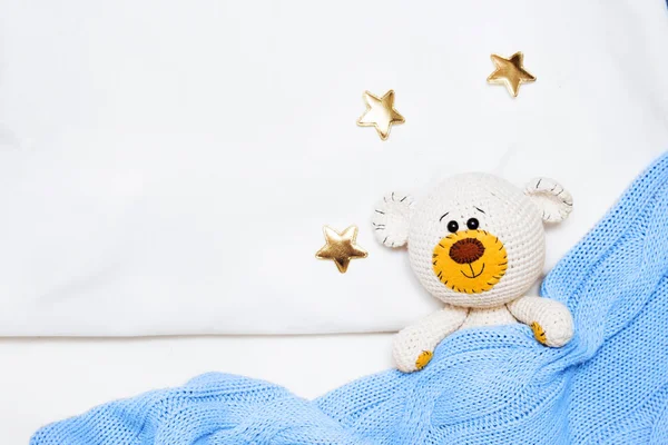 Un pequeño oso de juguete amigurumi de punto está cubierto con una manta azul, una cama plana, vista superior — Foto de Stock