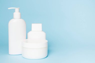 Mavi arka planda beyaz kozmetik kavanozları. Banyo aksesuarları. Yüz ve vücut bakım konsepti