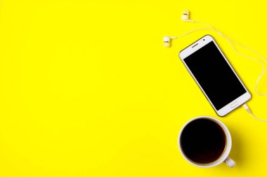 Akıllı telefon ve bir fincan kahve sarı bir arka plan üzerinde. Üstte görüntü.