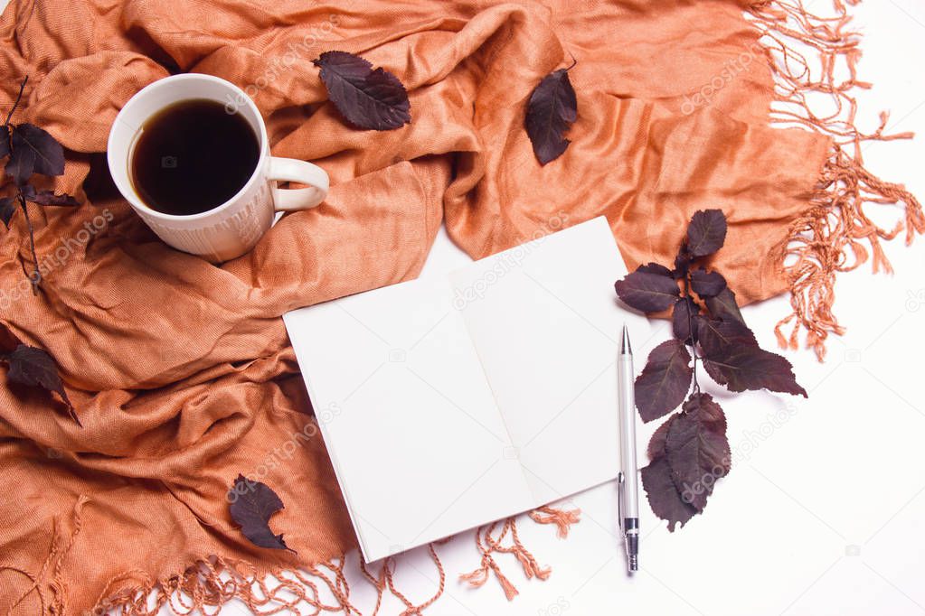 Autumn composition. A cup of coffee with a warm scarf, notepad and leaves on a white background. Autumn fall concept. Work desk. Top view, flat lay, copy space.