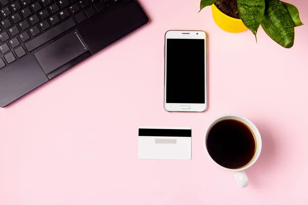 Akıllı telefon, klavye, bir fincan kahve ve pembe arka planda kredi kartı. Üst görünüm, iş konsepti