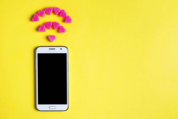 Top view of smartphone with the symbol of Wi fi from decorative hearts on yellow paper background. Internet technology and networking concept. — Stock Photo, Image