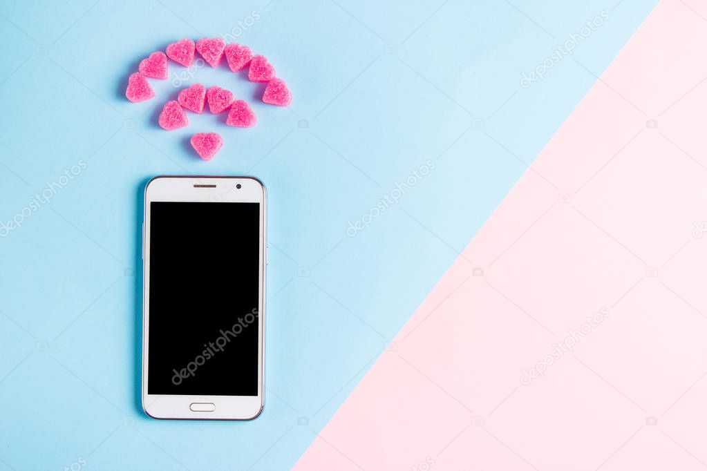 Top view of smartphone with the symbol of Wi fi from decorative hearts on art blue and pink paper background. Internet technology and networking concept.