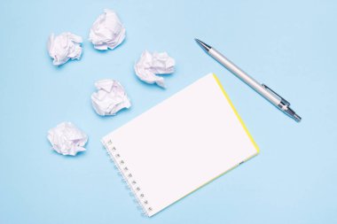 Mavi kağıt arka plan üzerinde boş defter, kalem ve buruşuk kağıt topları açın. Yaratılış süreci, fikir veya yaratıcı girişimleri kavramı. Kopyalama alanı.
