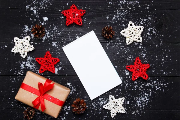 Composición navideña. Regalos de Navidad con estrellas decorativas rojas de ratán, conos y bloc de notas sobre fondo negro de madera. Vista superior, plano, espacio para copiar . —  Fotos de Stock