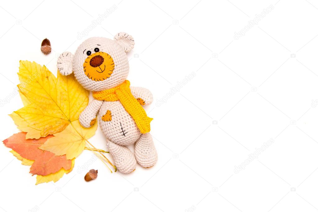 Amigurumi knitted teddy bear with autumn leaves isolated on white.