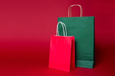 Kırmızı arka plan üzerinde iki noel kırmızı ve yeşil alışveriş kağıt torba. Alay etmek.