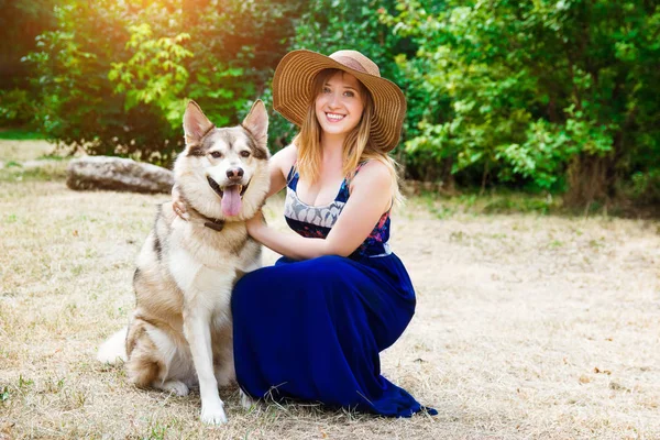 Happy young woman hugs siberian husky or malamute in the park. The concept of care and walking with a dog