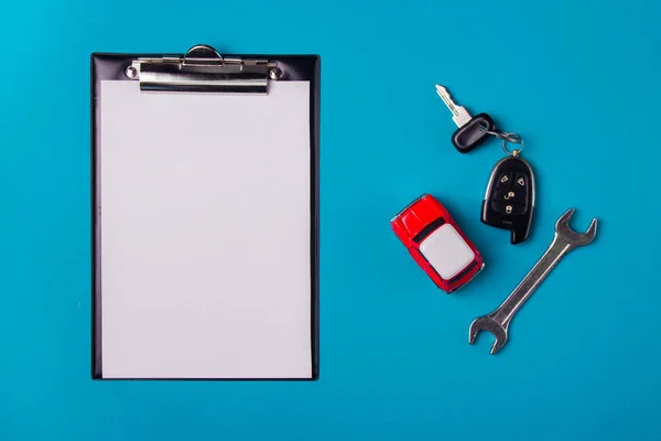 Paper blank with toy red car and keys on a blue background. Technical inspection or car credit concept. Top view and copy space.