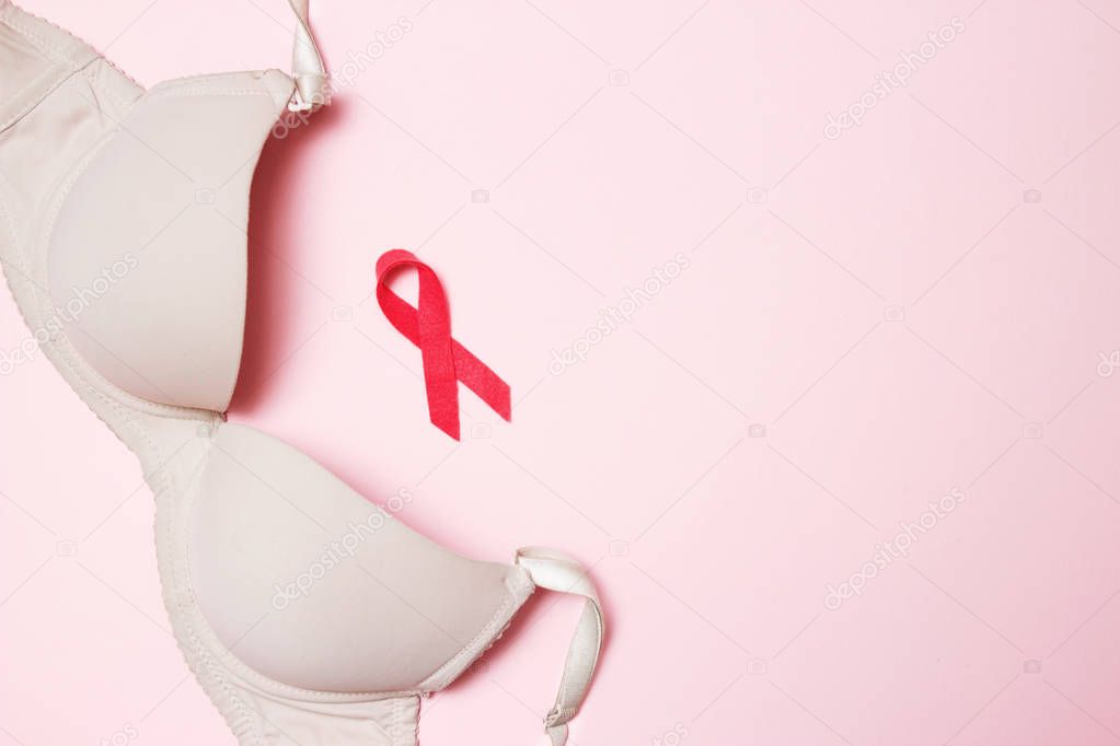 Bra with a symbol of the month of breast cancer awareness on a pink background top view, flat lay. Women's Health Concept.