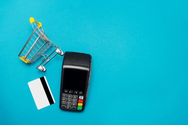 Mavi arka planda kredi kartı ve süpermarket arabası ile Pos ödeme terminali. Alışveriş online ve satış konsepti.