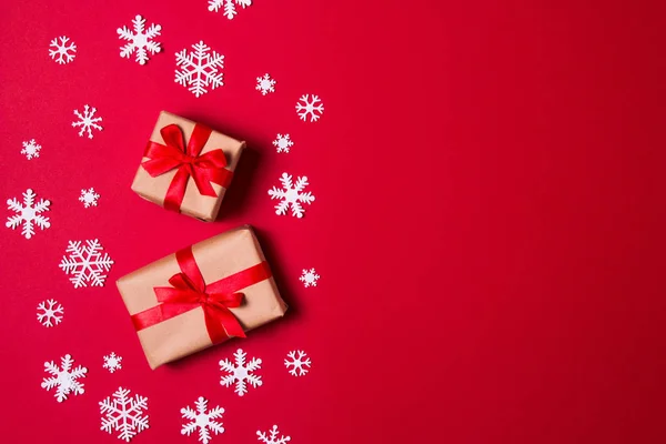 Tarjeta de felicitación de composición navideña. Regalo de papel artesanal sobre fondo rojo con copos de nieve. Vista superior, plano . —  Fotos de Stock